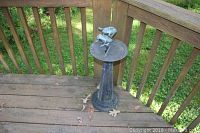 Full view of metal sundial lawn decoration on wooden deck corner showing frog figure on top and base.
