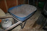 Full view of the blue metal wheelbarrow showing basin, frame, and front tire, dirt and wear visible.