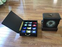 Photo showing the open wooden tea box with 12 compartments each holding differently colored tea packets, alongside the Sessions mantel clock with key on top.