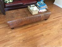 Leather ottoman positioned in living room area, showing tufted top and items placed on top.