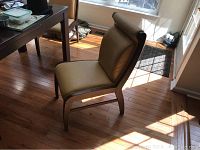 Side angle of one vinyl padded dining chair with wooden frame, muted yellow upholstery, curved legs, and cushioned seat and backrest.