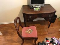 Desk and chair set in room with hardwood floor, showing desk surface, chair with pink floral needlepoint seat and carved backrest.