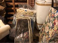 Photo showing a stack of multiple twin-sized comforters and quilts in clear plastic storage bags with floral and dark patterned textiles.