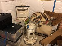 Full view of propane heater surrounded by plastic containers, GoldStar dehumidifier box, Honeywell fan, and textiles.