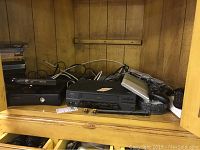 Xbox 360 console, Panasonic 4-head VCR, assorted controllers and cables inside a wooden cabinet.