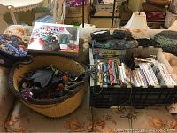 Overview photo showing the basket with Skylanders figures, Spyro's Adventure carrying case on top, and crate holding multiple game cases with controllers and cables on a floral couch.