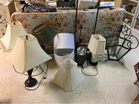 Photo showing the six lamps including three table lamps with shades, two floor lamps, and one chandelier on the floor near a floral couch.