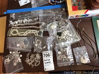 Overview of all jewelry items showing multiple strands, earrings and bracelets in plastic bags on table.