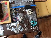 Overview of various bracelets, necklaces, rings, and earrings laid on table including some stored in plastic bags.