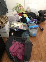 Photo showing assortment of items including backpack, stuffed animal, exercise weights, blanket, and bags on floor.