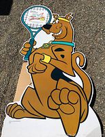 Full view of Scooby Doo cardboard stand-up showing Scooby holding a tennis racket with yellow wrist and head bands, sitting position.