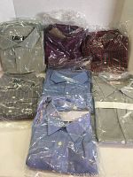 Seven folded men's shirts in various colors and patterns, mostly in plastic wrapping.