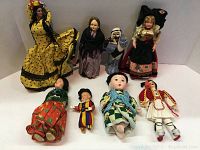Full view of all 8 vintage international dolls arranged in two rows on a white surface showing various cultural costumes