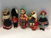 Five vintage international dolls displayed in a group, showing full body and costumes, standing on white background.