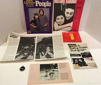 Photo of all collectible items arranged: People Magazine John Lennon tribute issue, Instant Karma sheet music, Beatles charm, Beatles & Rolling Stones photographs brochure, open magazine article with Beatles photos, and text.