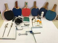 Photo showing 6 paddles, 2 nets including a rolled one labeled STIGA, 3 metal net holder sets, and 15 ping pong balls scattered on flat surface.