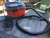 Full view of the Craftsman Shop Vac on a table outside showing the red tank, gray motor housing, attached power cord, and flexible plastic hose.