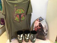 Photo of olive green Star Wars T-shirt with Boba Fett helmet graphic, three large Star Wars plastic cups, and Star Wars swimming kickboard with Kylo Ren and Stormtroopers