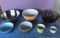 Photo showing all seven bowls lined up on a blue cloth: large metal bowl, orange Pyrex, smoke-colored glass, and four smaller bowls in blue, brown, green, and white.