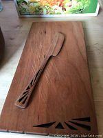 Teak wooden cutting board with carved wooden knife resting on top, showing condition and details of knife design.