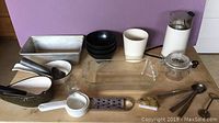 Photo showing all kitchen tools and accessories including Braun coffee grinder, bowls, baking pans, measuring tools, and utensils arranged on table.