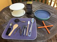 Photo of all kitchen items arranged on a purple cloth mat including utensils, turquoise blue bacon grilling pan, coffee grinder, and trivet.