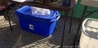 Blue Sterlite plastic storage bin shown outdoors under table with loosely fitting lid.
