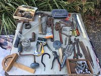 Various vintage hand tools including wrenches, hammers, screwdrivers, a hand drill, staple gun, and hardware laid out on a table.