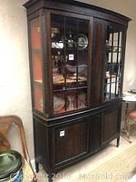 Front angled view showing glass paneled upper display cabinet and solid wood lower storage with visible orange felt shelves inside