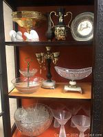 Glass cabinet showing glassware and decorative brass items, including punch bowl set and serving dishes