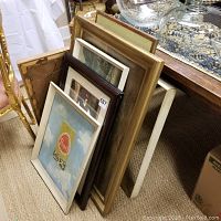 View of two signed paintings stacked with two empty frames and a Pearl Beer painting leaning against a piece of furniture.
