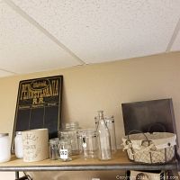 Shelf display showing railway station board, ceramic cookie jar, white mason jars, locking glass pantry jars, vintage floral glass bottle, and wire linen basket.