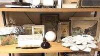 Shelf with multiple art pieces including framed prints, stone flower pieces, marble ball, crystal vase, and decorative glass bird.