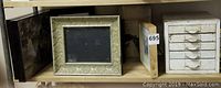 Shelved frames and prints of various sizes including a wooden frame and metallic frame.