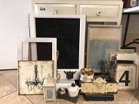 Photo showing the cream wooden table with two drawers behind a collection of decorative and vintage items including a chalkboard, washboard, figurines, and framed artwork.