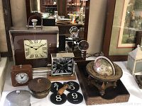 Photo showing three clocks (large leather clock, medium wooden clock, small faux leather clock), decorative objects, black type-font coasters, vintage wooden globe with zodiac signs, and wooden letter box tray