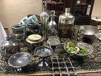 Photo showing collection of metal containers, jars, silver plated trays, glass bottles, and metal bowls on patterned surface.