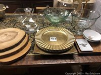 Wide view of the lot showing wood slices, decorative metal plates, square and round ceramic dishes with insect designs, and various glass bowls and drinking glasses arranged on a patterned surface.