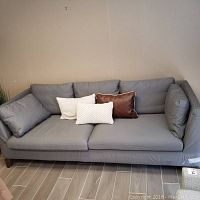 Full view of grey fabric sofa with three pillows, showing overall design and condition.