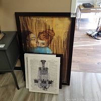 Full view of signed painting of stylized portrait of two people and three framed prints of chandelier illustrations on vintage dictionary pages.