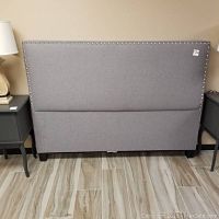 Front view of the grey upholstered headboard showing its rectangular shape and nailhead trim along the edges.