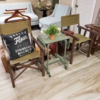 Two vintage directors chairs, a metal medical rolling table with pop-up sides, glass jar, and small basket arranged together on a tiled floor.