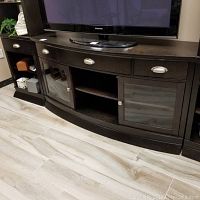 Full view of dark wooden media cabinet with three drawers and two glass doors beneath a flat screen TV.