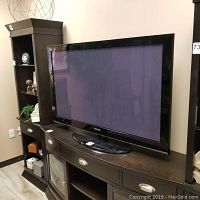 Front view of Samsung flat screen TV sitting on dark wooden cabinet, showing black bezel and base stand.