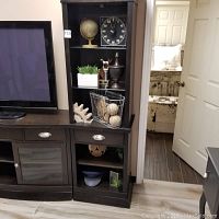 Full view of wooden shelving unit with metal wire basket holding wooden gear decor and sports items. Adjacent TV stand, couch partially visible.