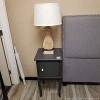 Side view of dark grey wooden side table next to a grey upholstered headboard with lamp on top