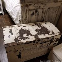 Closed view of rectangular wooden chest with heavily chipped white paint and metal hardware.