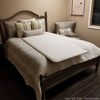 Full view of wooden bed with bedding and pillows, room setting with chair and wall art