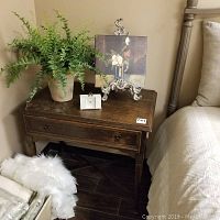 Vintage wood table next to bed with faux fern plant, leather clock, and canvas art.