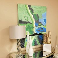 Photo showing the full scene of the signed abstract painting on canvas behind the glass lamp with stacked spheres base, two white ceramic vases, and a cube vase holding wood trunks.